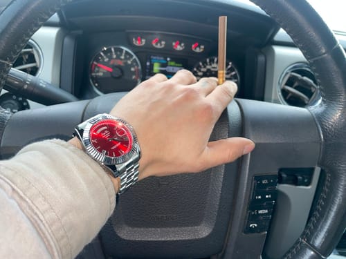 Customer's hand on a steering wheel, wearing the crimson Lucky Fours® Santos watch with a silver band.