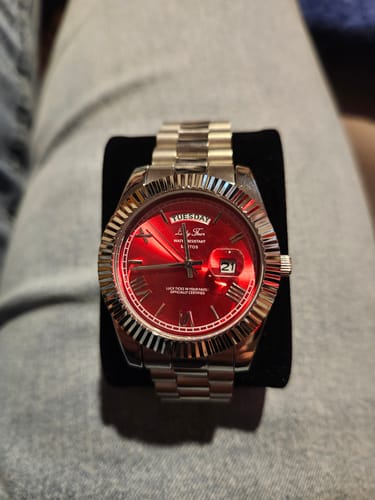 Customer's silver Lucky Fours® Santos watch with a vibrant red dial and fluted bezel, resting on a black stand.