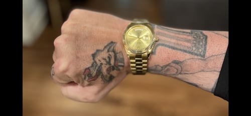 Reviewer showing their gold Lucky Fours® Santos watch on their tattooed wrist.