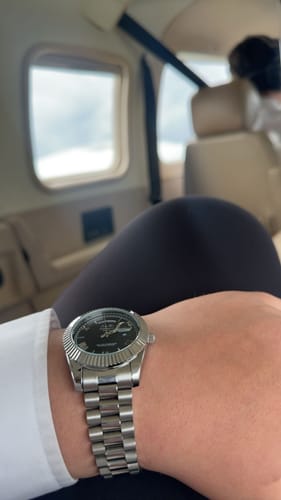 Close-up of a reviewer wearing the silver-colored Lucky Fours® Santos watch on their wrist inside an airplane.